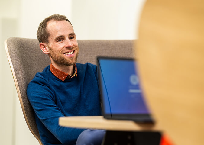 Laptop placed on a table beside a seated person in a modern workplace seating area.