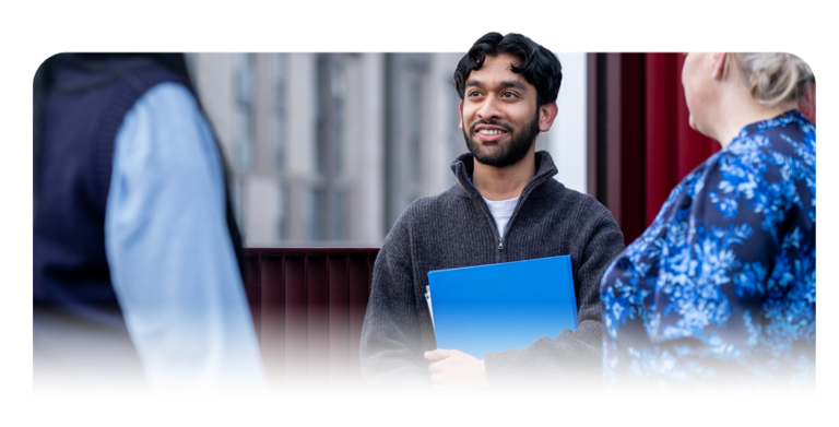 Person holding a blue folder while standing and speaking with two others.