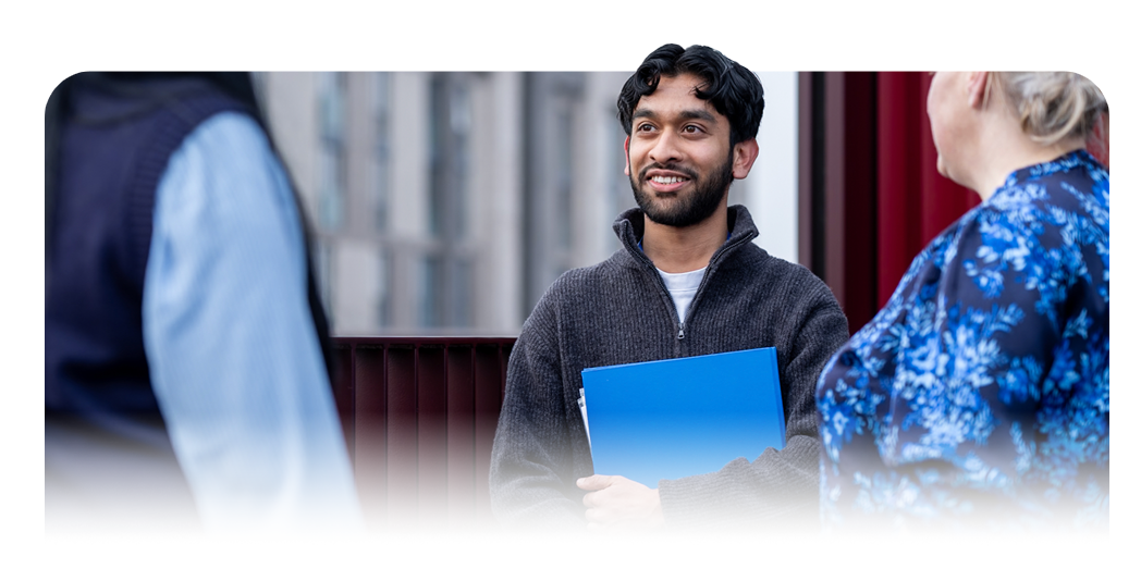 Person holding a blue folder while standing and speaking with two others.