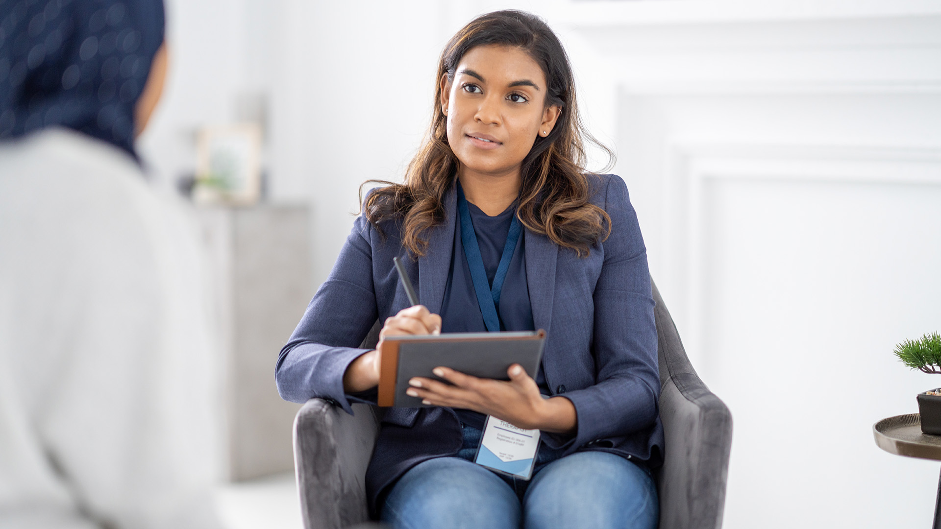 Person seated indoors with a tablet, facing another person out of view.