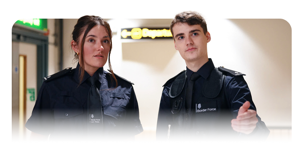 Two uniformed Border Force Officers standing in a corridor, with 'Departures' signage visible in the background.