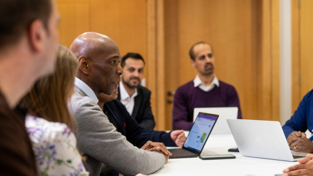 Several people seated around a table using laptops during a meeting.