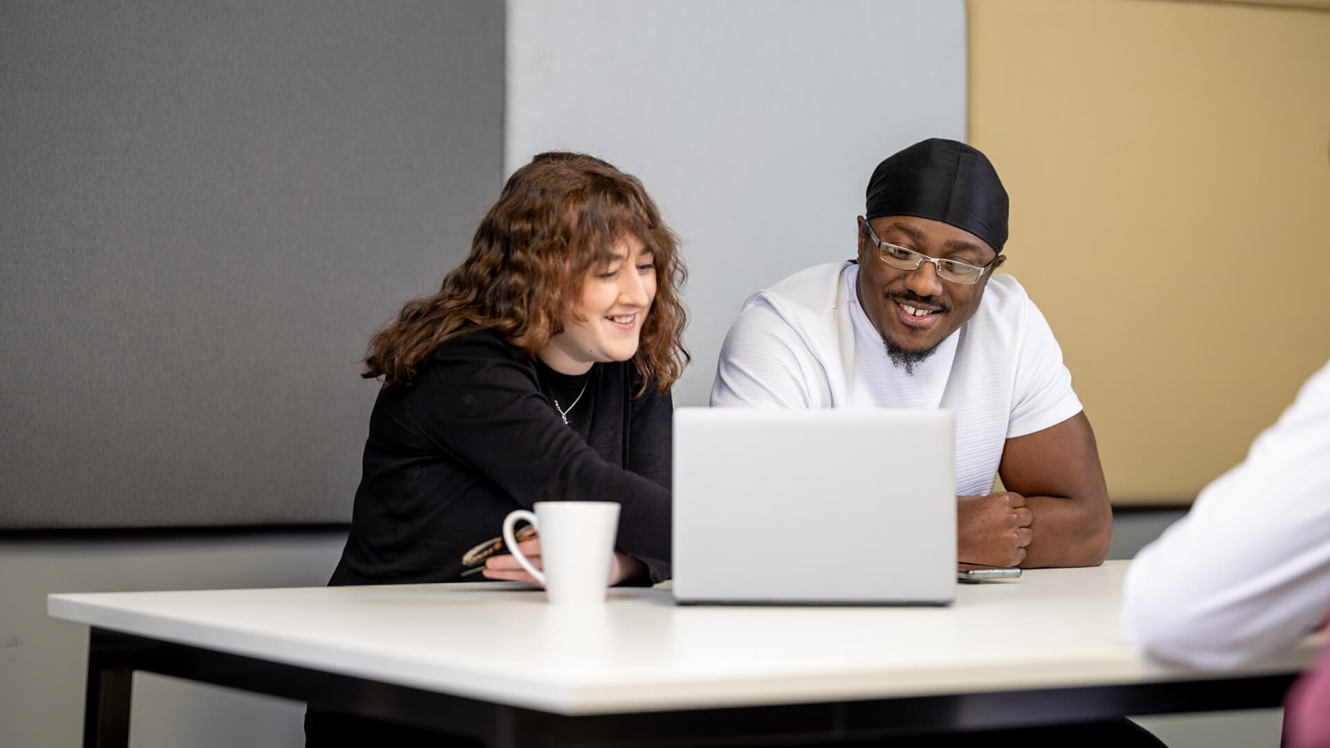 Two people seated at a table, looking at a laptop together.