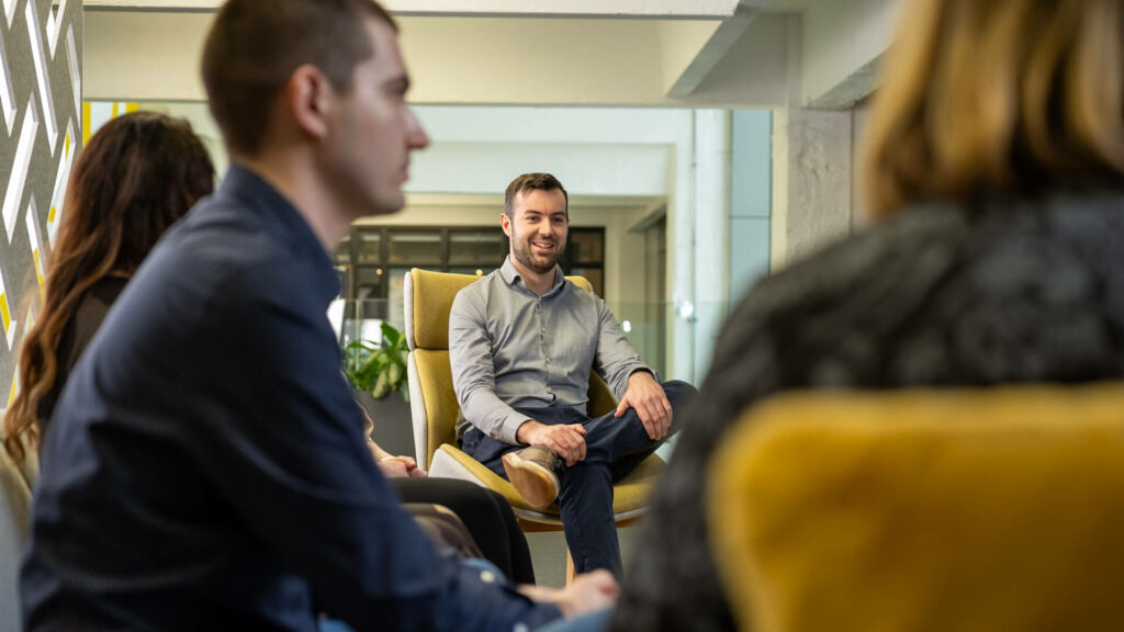 People seated in armchairs, one person centred with others partially visible.