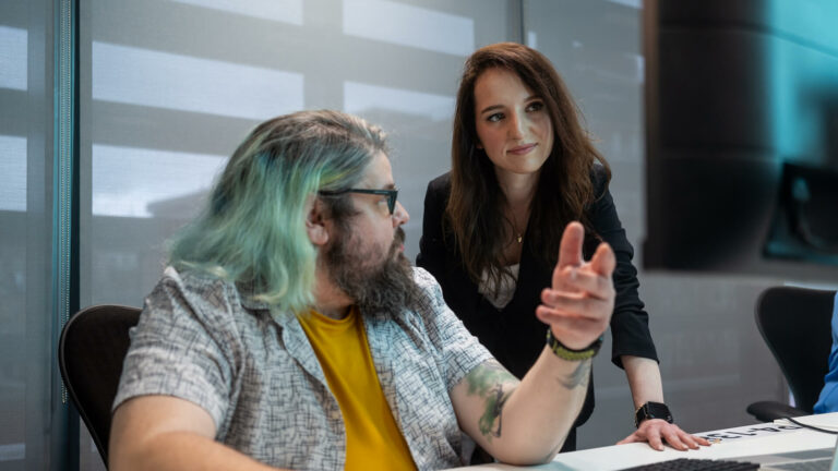 Two people at a desk discussing content on a computer screen.