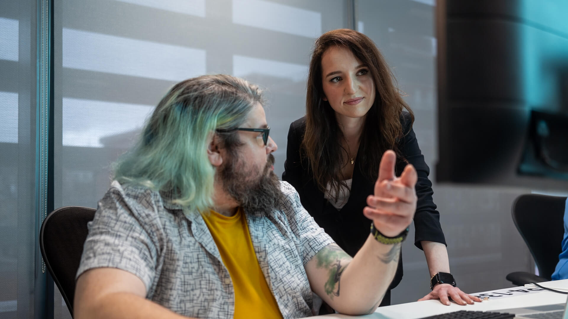 Two people at a desk discussing content on a computer screen.