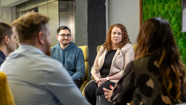 Office lounge area showing people seated and facing each other in discussion.