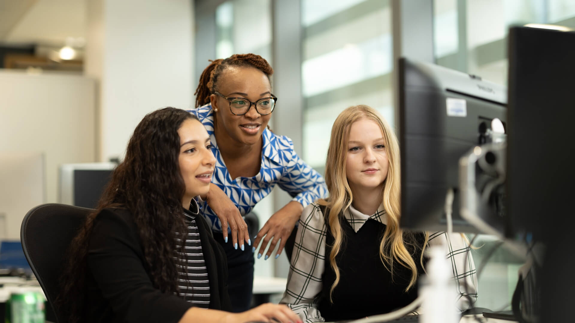 Workspace environment with three people at a workstation viewing content on a screen.