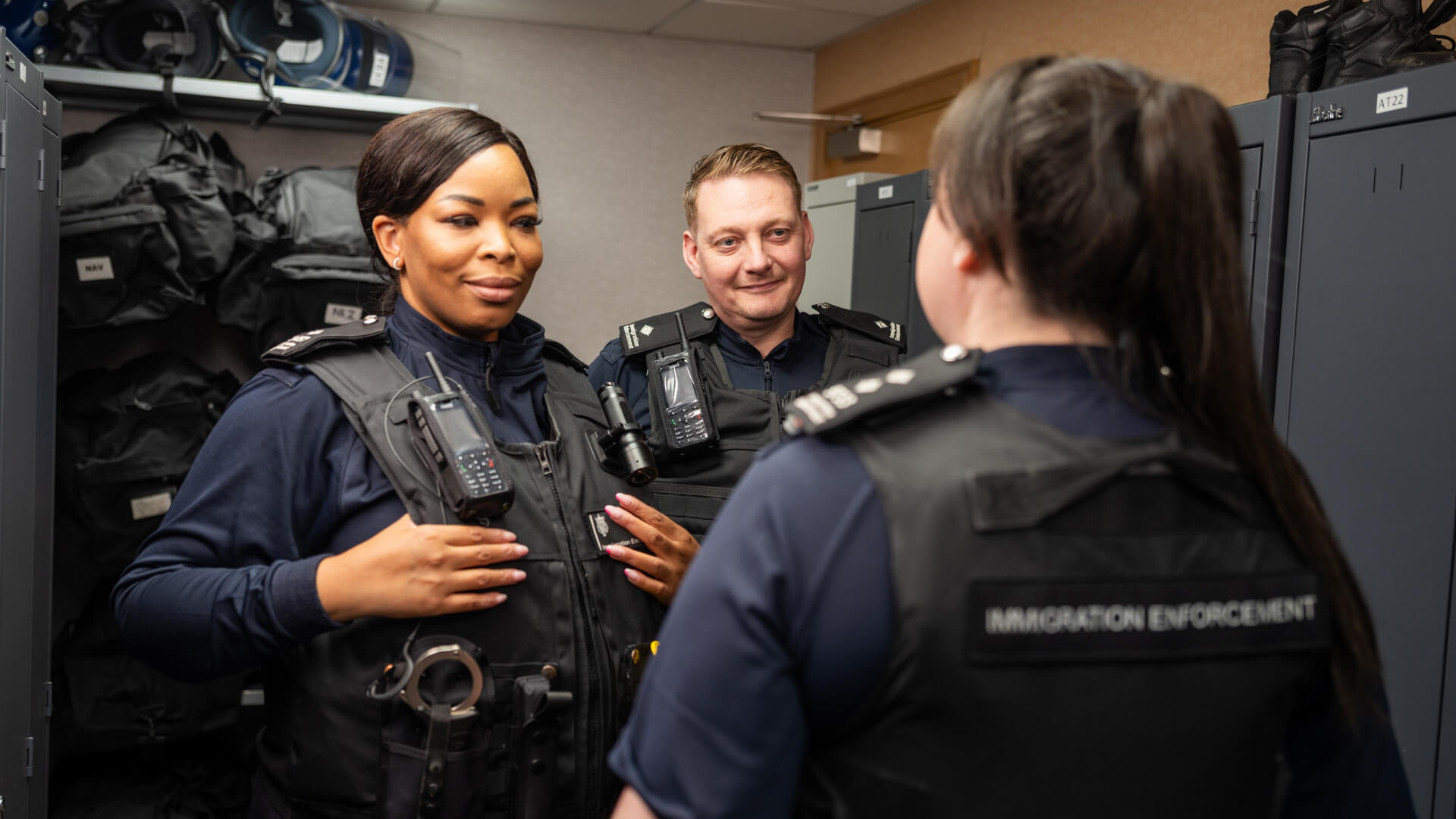 Three Immigration Enforcement Officers stood in a locker room.