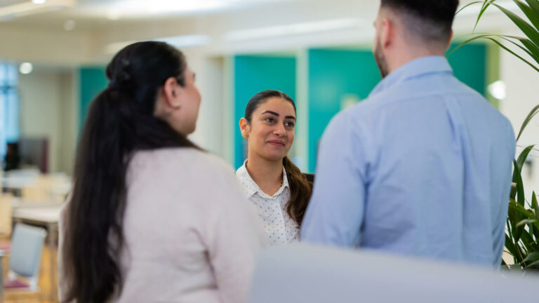 Three people standing in a modern office, facing each other in conversation.