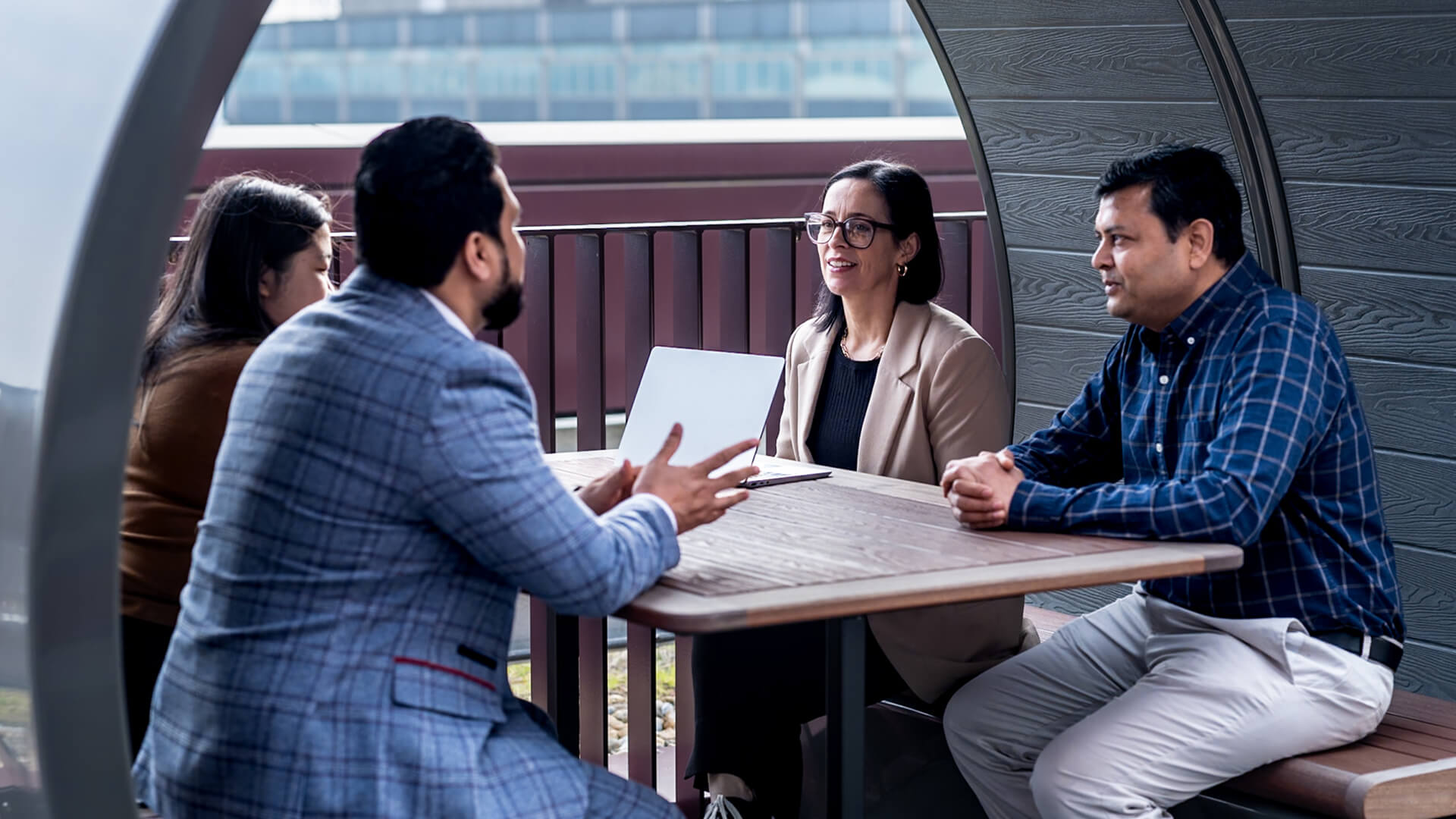 Outdoor seating area showing four people seated around a table, with a laptop placed between them.