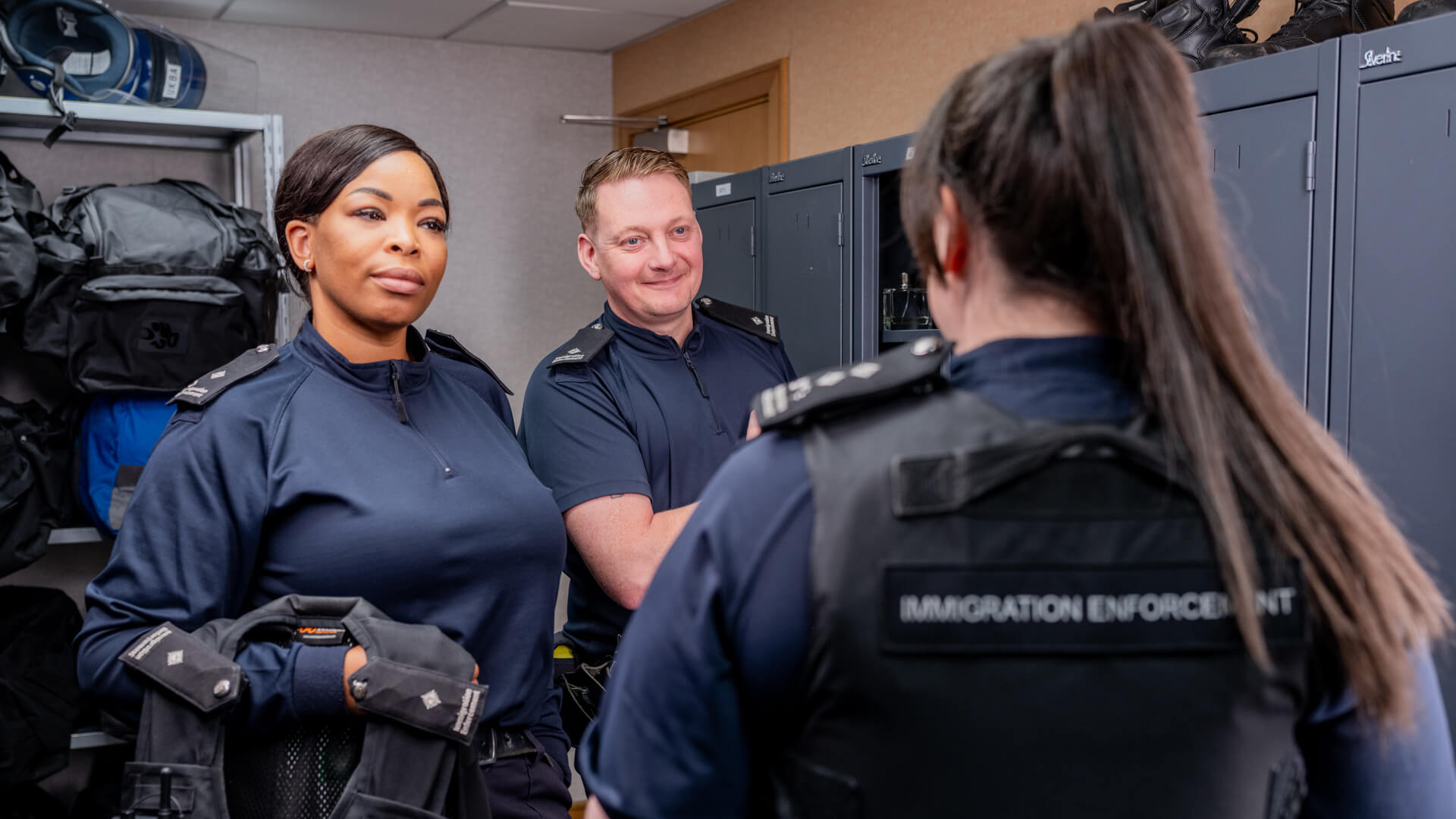 Three Immigration Enforcement Officers stood in a locker room.